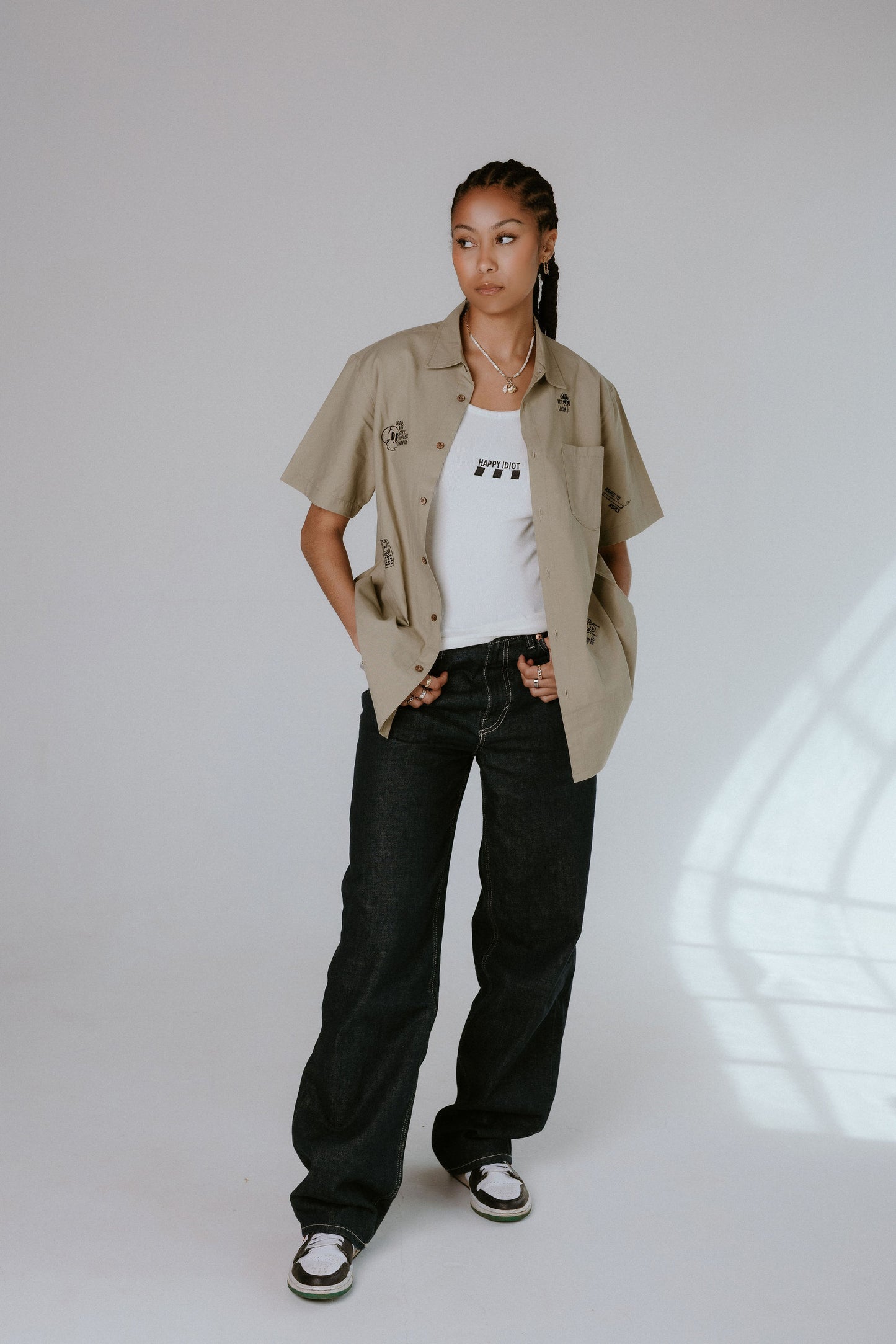 Person wearing a beige shirt, white t-shirt, black jeans, and black and white sneakers on a light background
