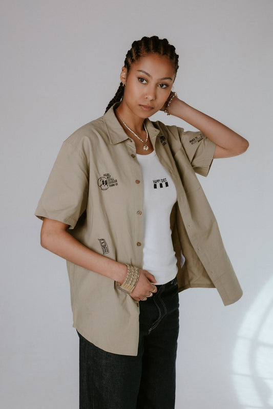 Person wearing a beige shirt over a white top with text, standing against a plain background